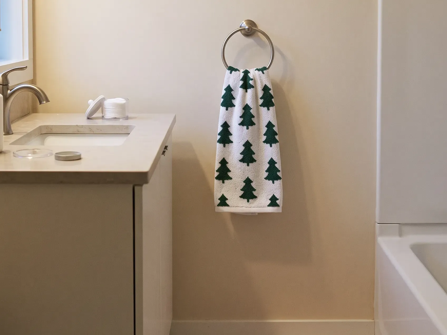 Green and white tree hand towel hanging on a towel ring on the wall beside a vanity with a basin and tap, Christmas bathroom towels in a small bathroom