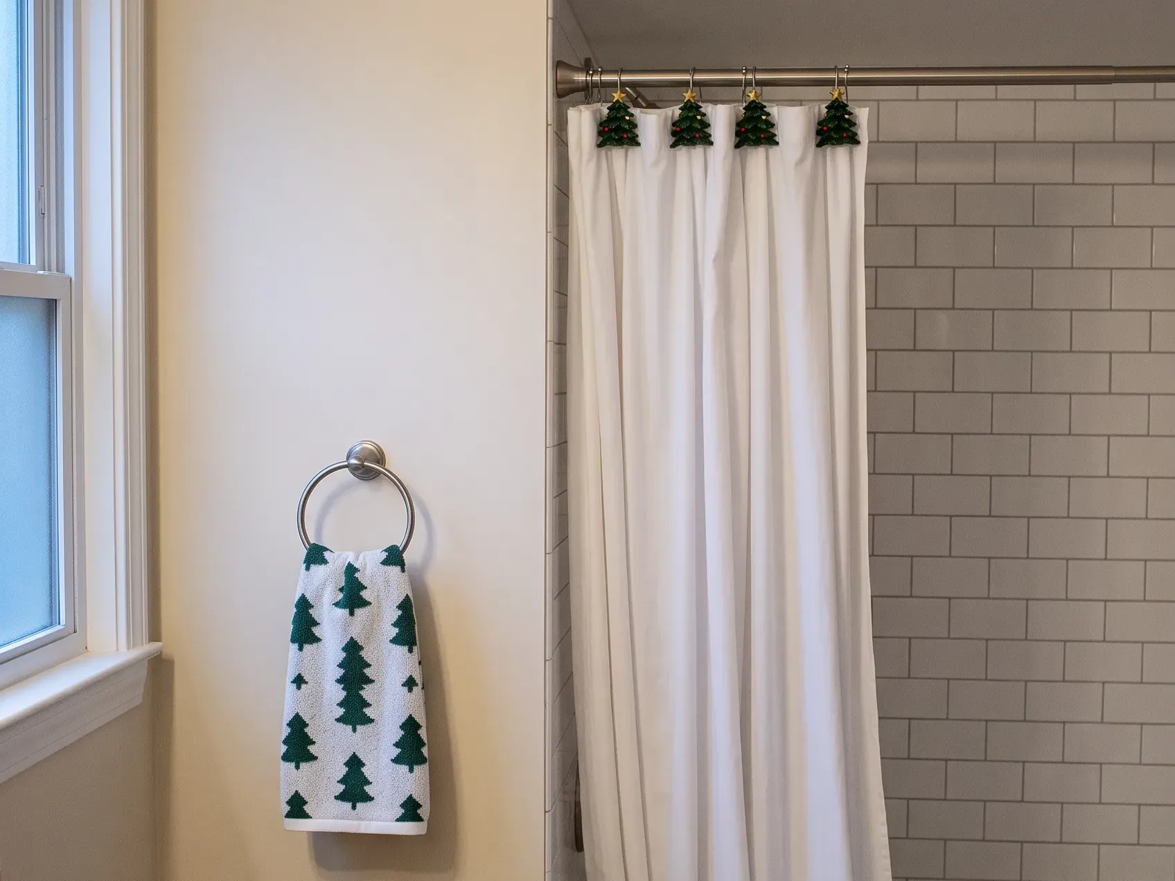 Corner of a small bathroom where the shower rod meets the wall, a plain white curtain hanging from green tree-shaped hooks with gold stars above a green and white tree hand towel on a towel ring, a green and white Christmas bathroom palette