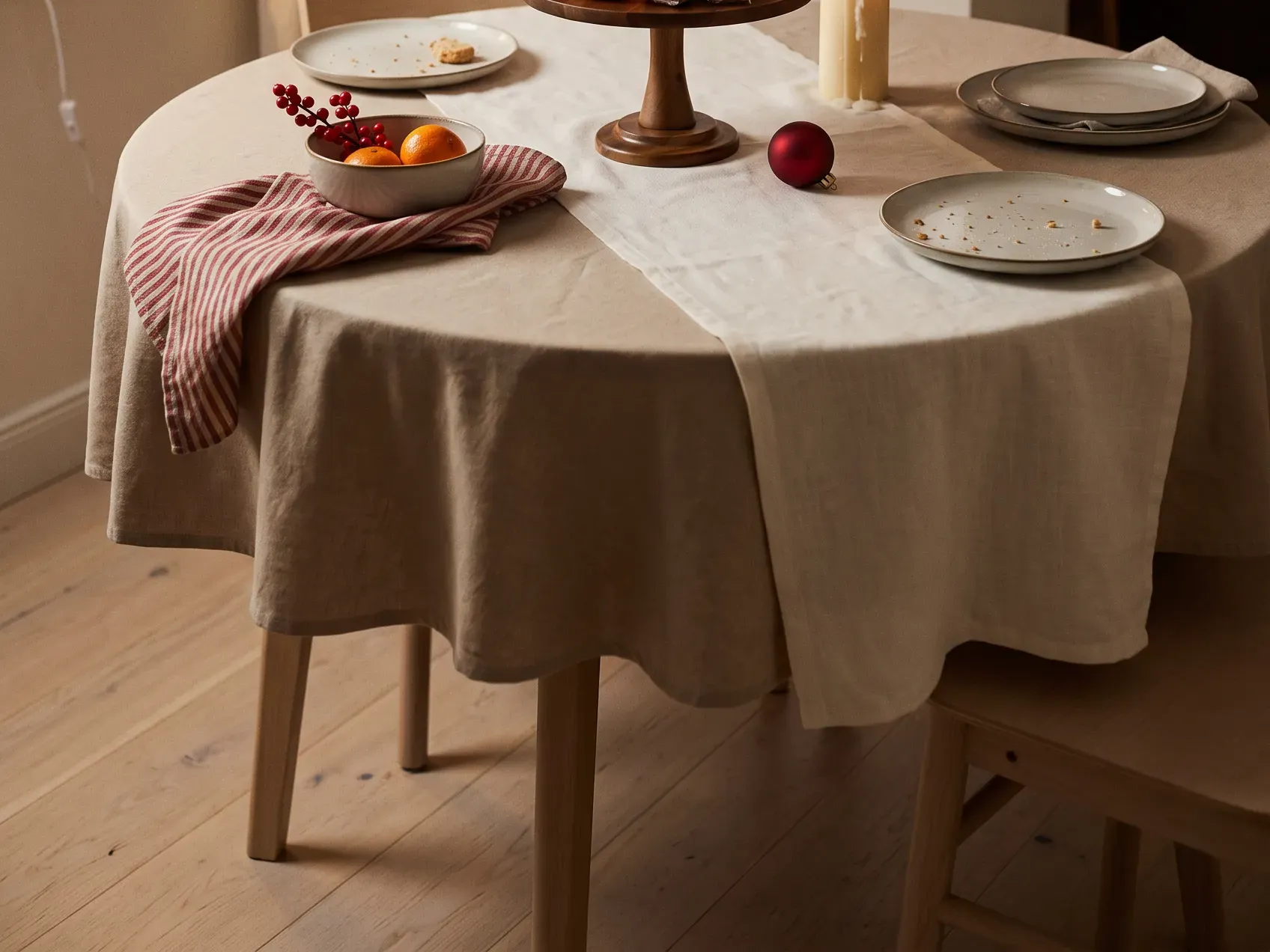 Round acacia wood cake stand raised on a pedestal holding small items in the center of a set apartment table, a vertical Christmas table centerpiece