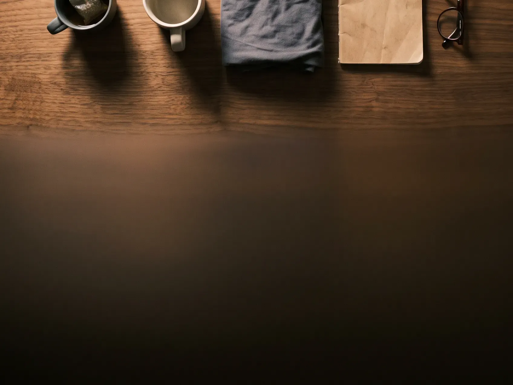 Two mugs and a small stack of folded fabric on a wooden table with an empty basket nearby, editing down a cozy night in gift basket
