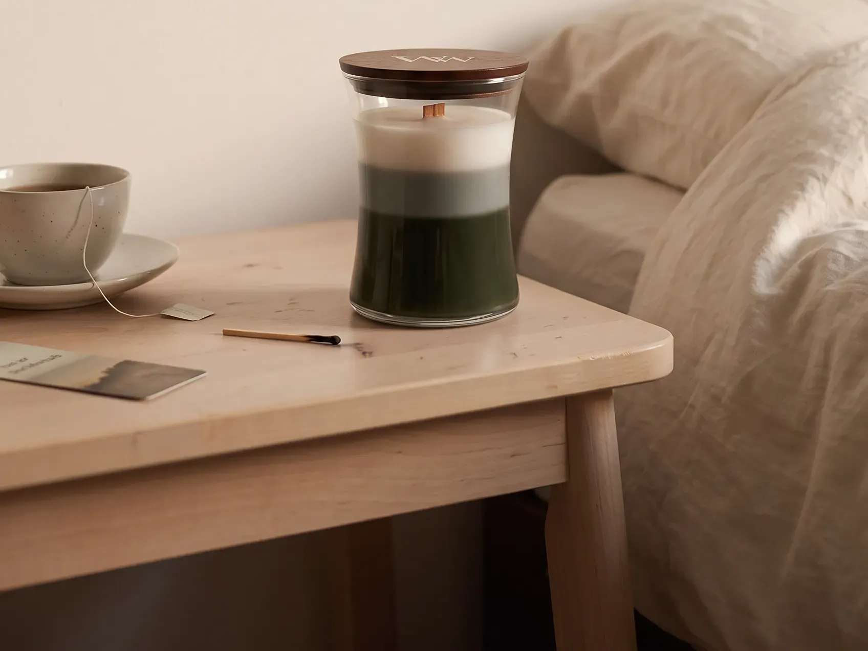 Wood wick candle and a tea cup on a bedside table at night, fall bedroom decor for a rental