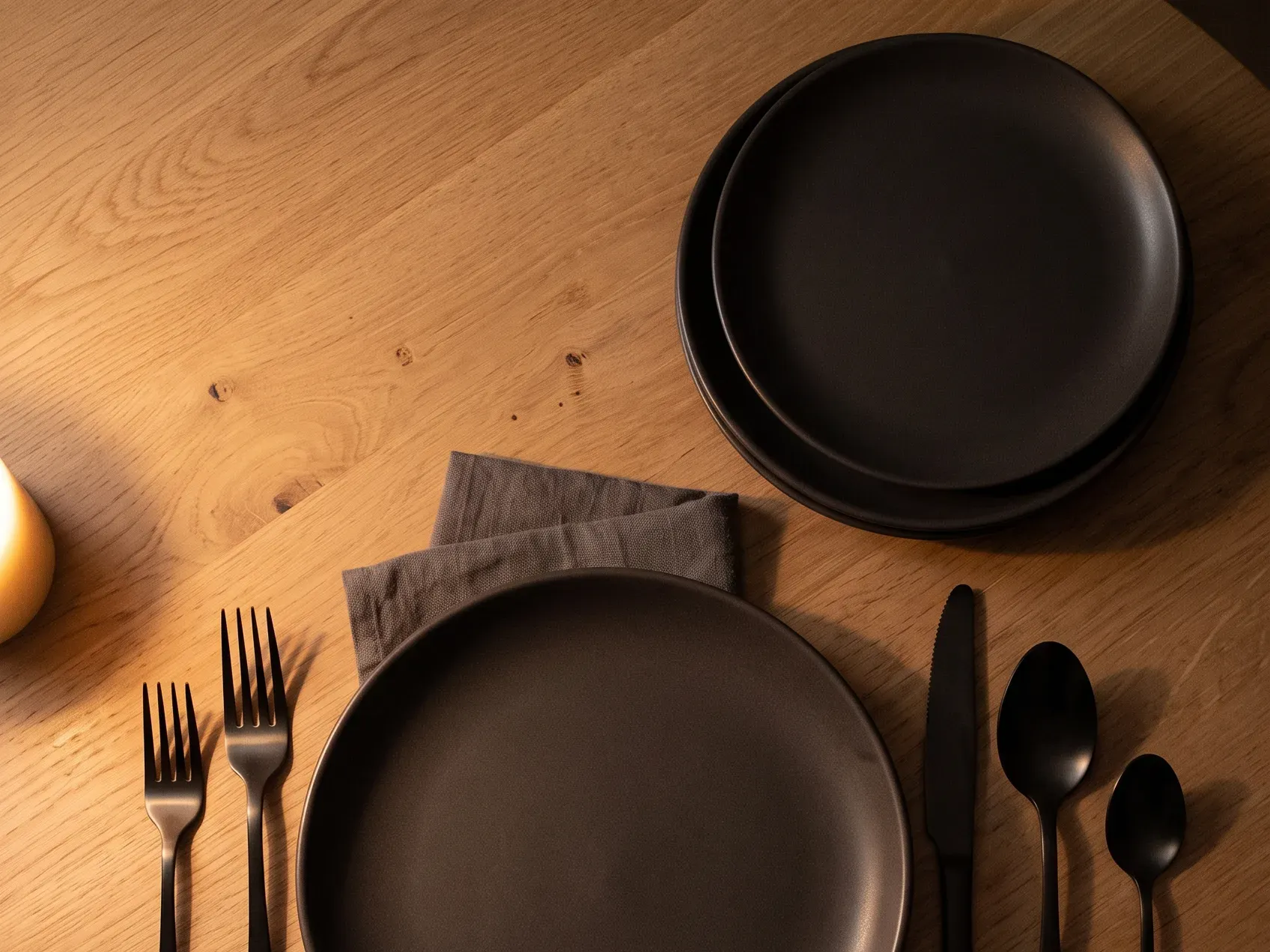 Matte black fork, knife and spoon laid beside a charcoal plate on a dark woven mat, Halloween table decor that stays useful after the season