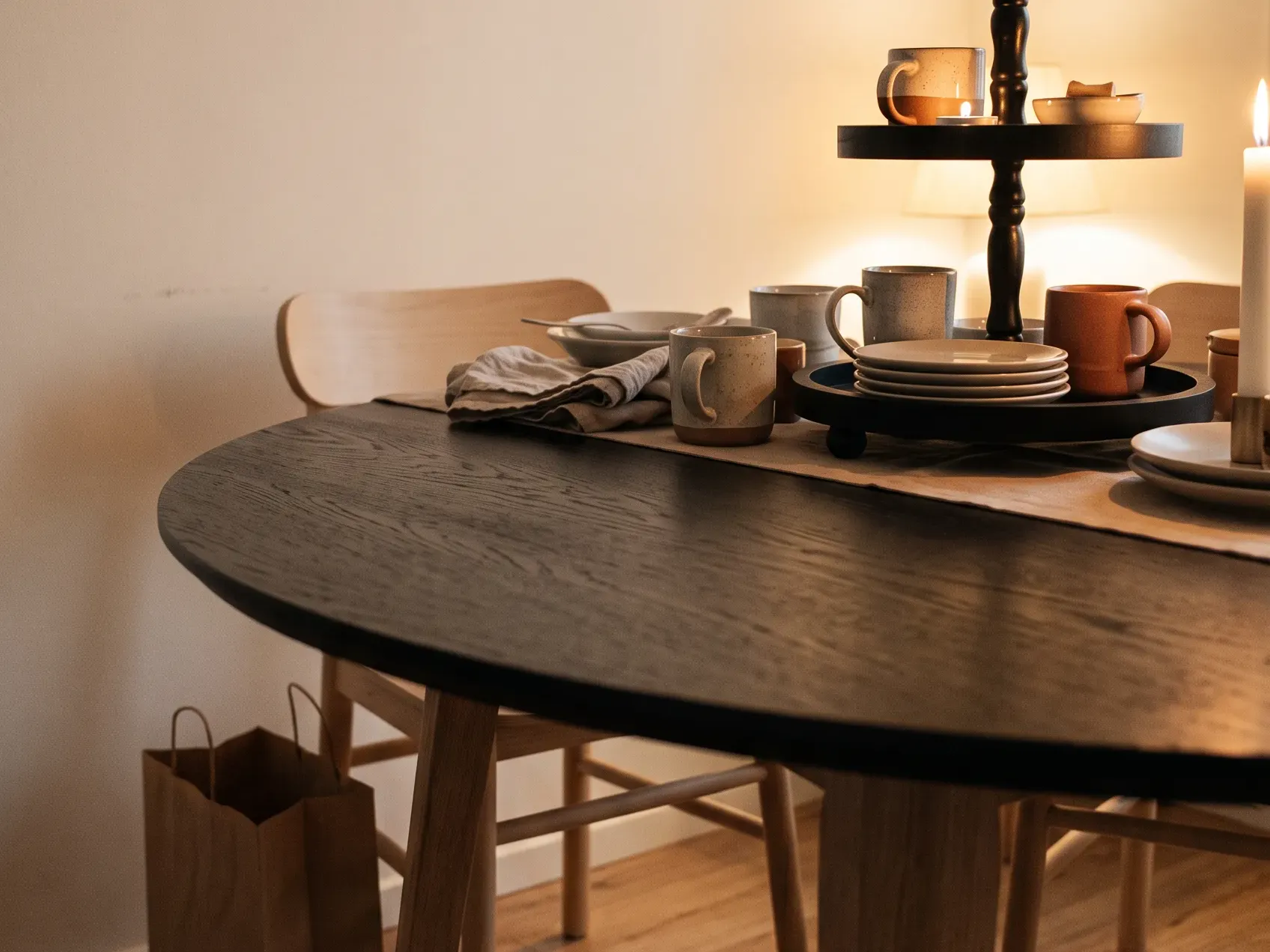 Apartment dining table half cleared with a black tiered tray pushed to one end and bare wood left free, small-space Halloween table decor that packs down