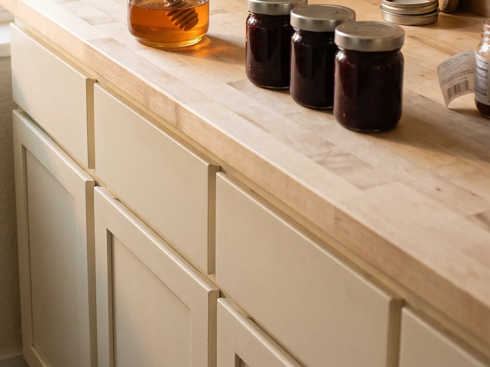 A glass honey jar with a wooden dipper, a jam variety trio and a travertine match holder grouped on a kitchen counter, last-minute hostess gift ideas