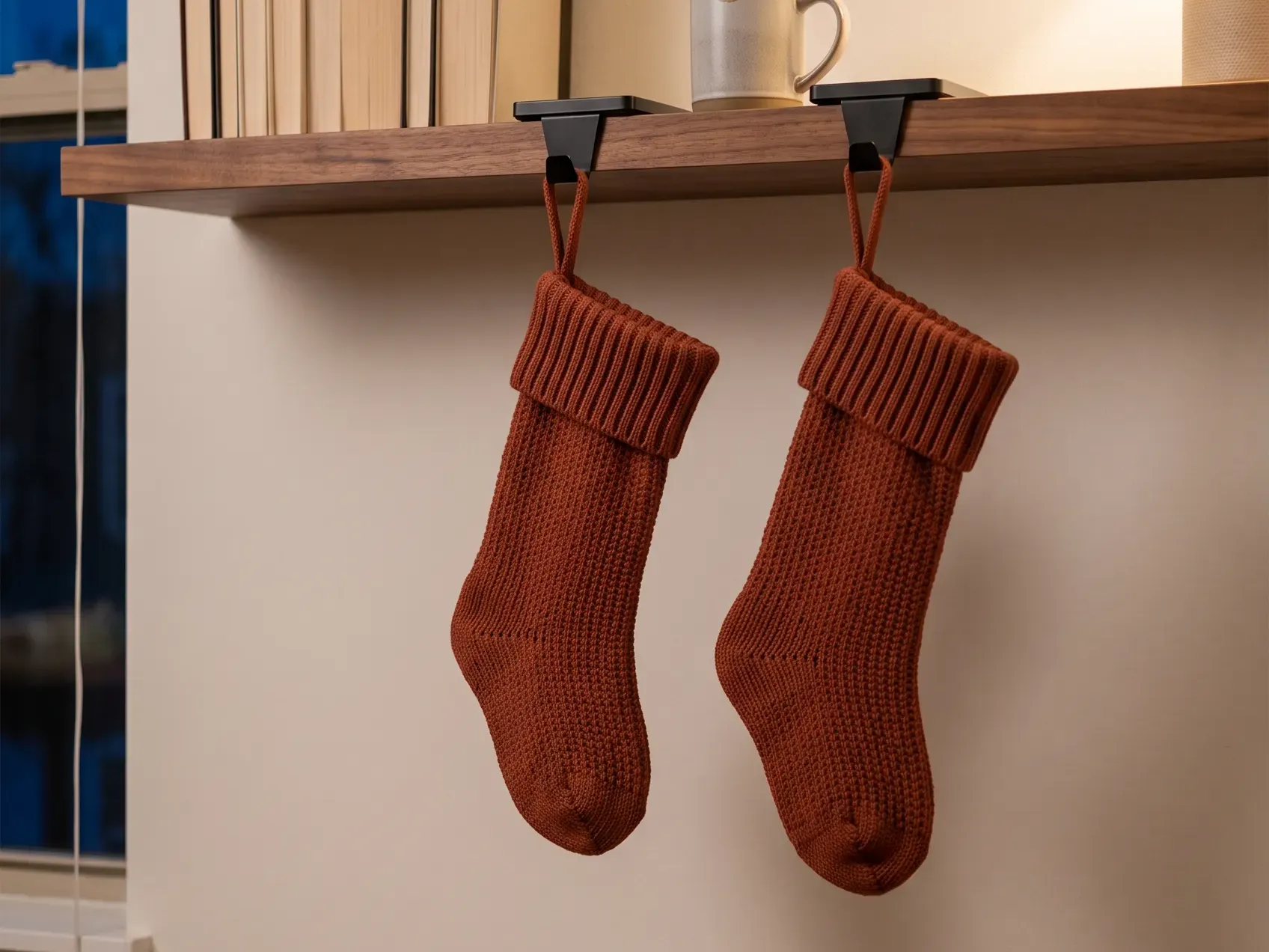 Two knit stockings hanging from weighted metal stocking holders on the edge of a console table in a small apartment, a mantel-free Christmas decor idea for renters